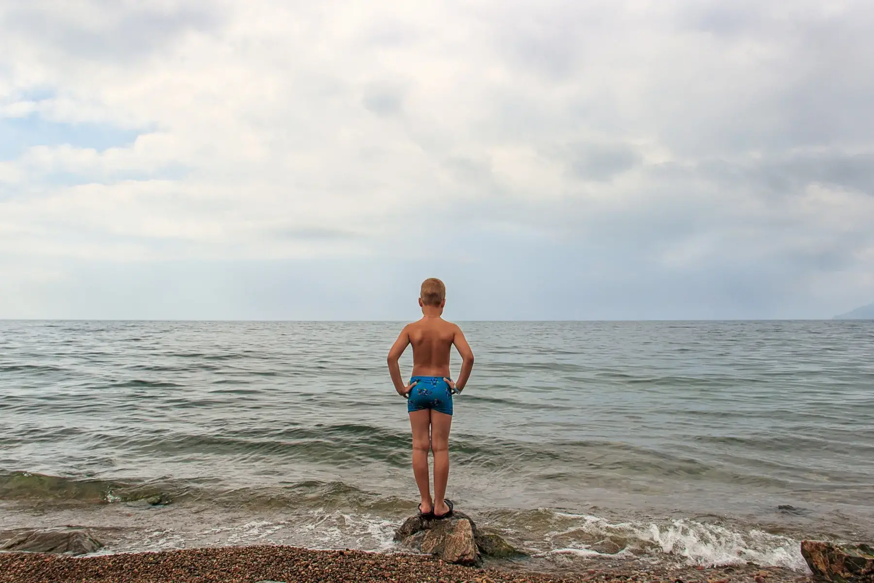 Pojke i badbyxor står intill havet.
