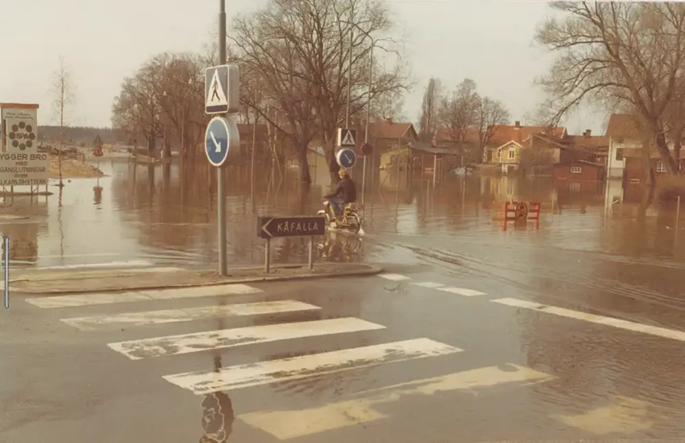 En moped plöjer genom decimeterhögt vatten vid översvämning i Lindesberg 4 maj 1977.