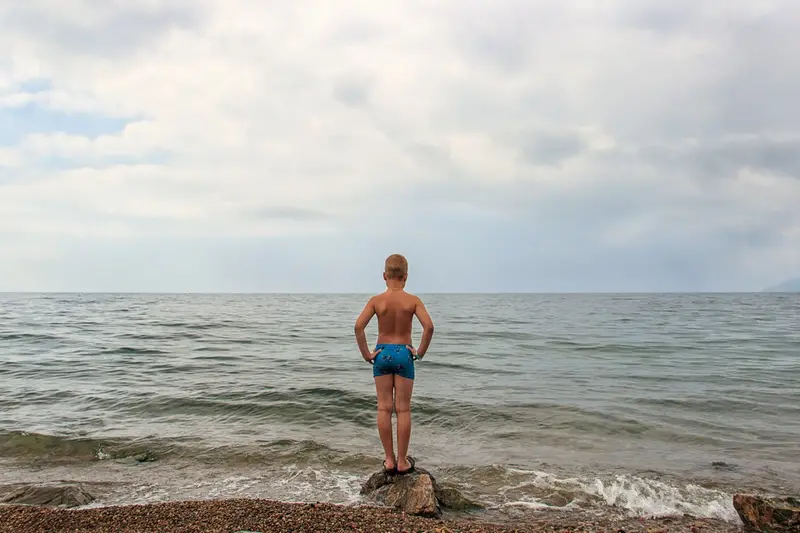 Pojke i badbyxor står intill havet.