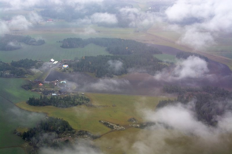 Flygbild över grönskande landskap genom moln.