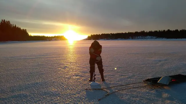 Solnedgång vid en istäckt sjö där en person mäter isen.