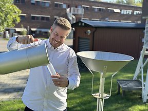 Bild på en man i ljus skjorta som demonstrerar nederbördsmätning vid en mätstation. 